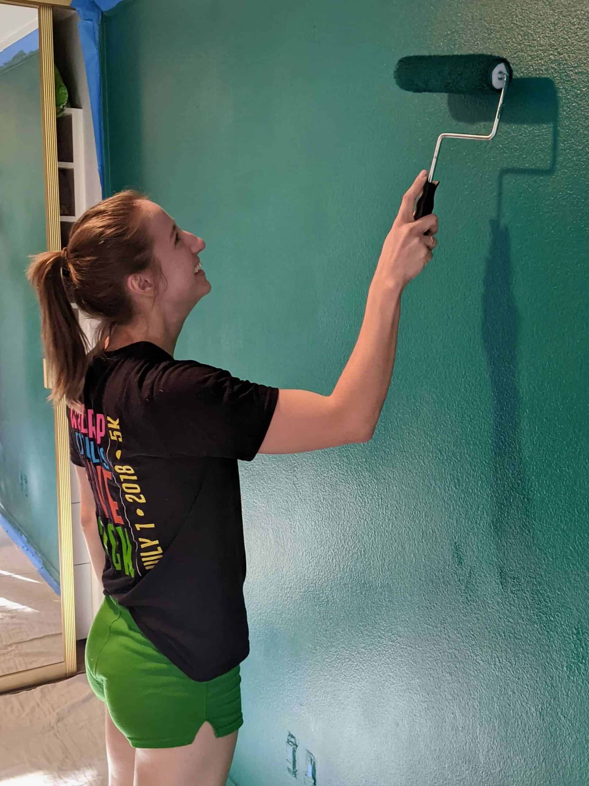 Woman holding a paint roller and painting a wall teal.